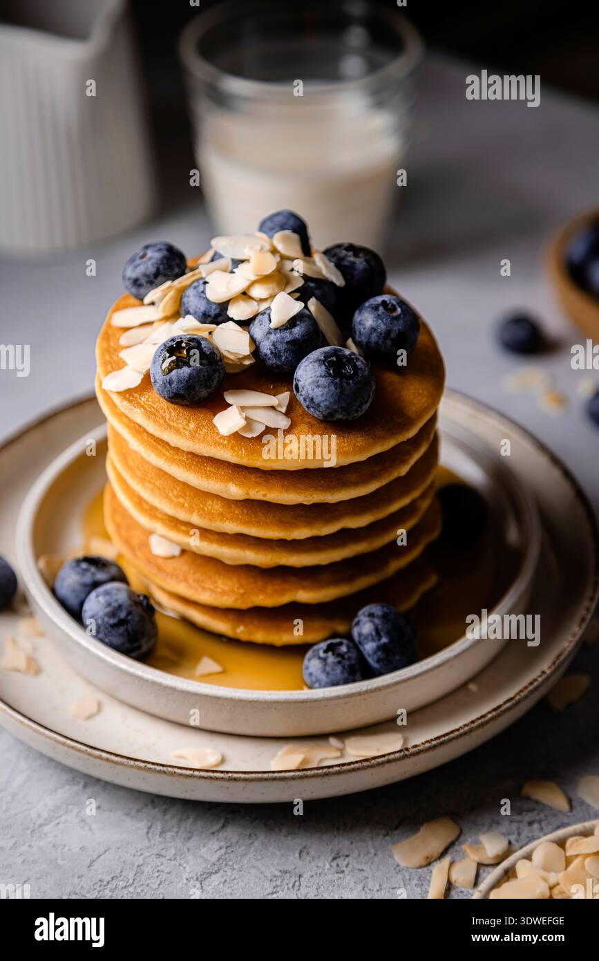 Deliziosa colazione con una pila di soffici pancake ricoperti di mirtilli freschi e mandorle a scaglie. Le frittelle sono ricoperte di sciroppo, aggiungere Foto Stock