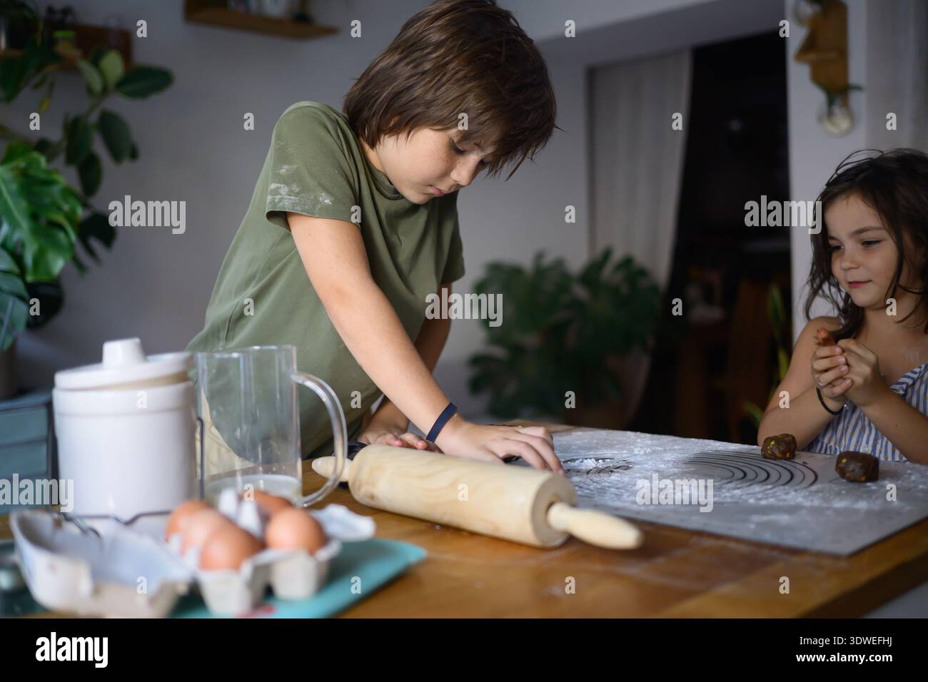 Due bambini amano imparare e cucinare insieme in cucina. Stanno preparando biscotti, circondati da ingredienti e strumenti, catturando l'essenza del chi Foto Stock