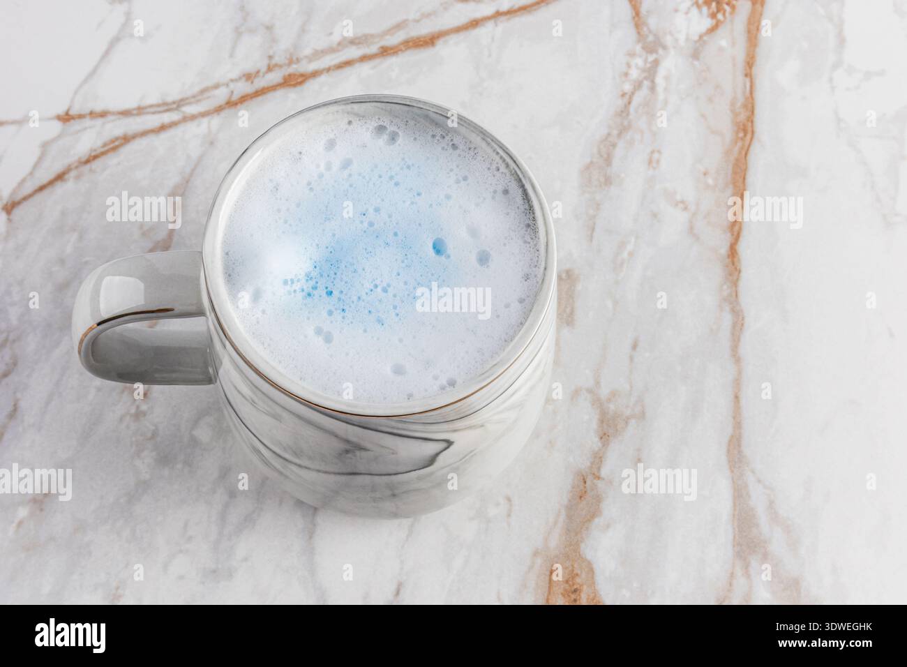 Un latte matcha blu cremoso servito elegantemente in una tazza decorata in marmo, posta su un tavolo in marmo lucido. Il rilassante tocco blu esalta la pace Foto Stock