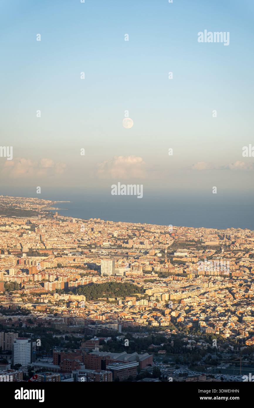 Splendida vista aerea di Barcellona da Tibidabo mentre il sole tramonta, illuminando il paesaggio urbano con un caldo bagliore. Il mare e l'orizzonte distante migliorano il Foto Stock