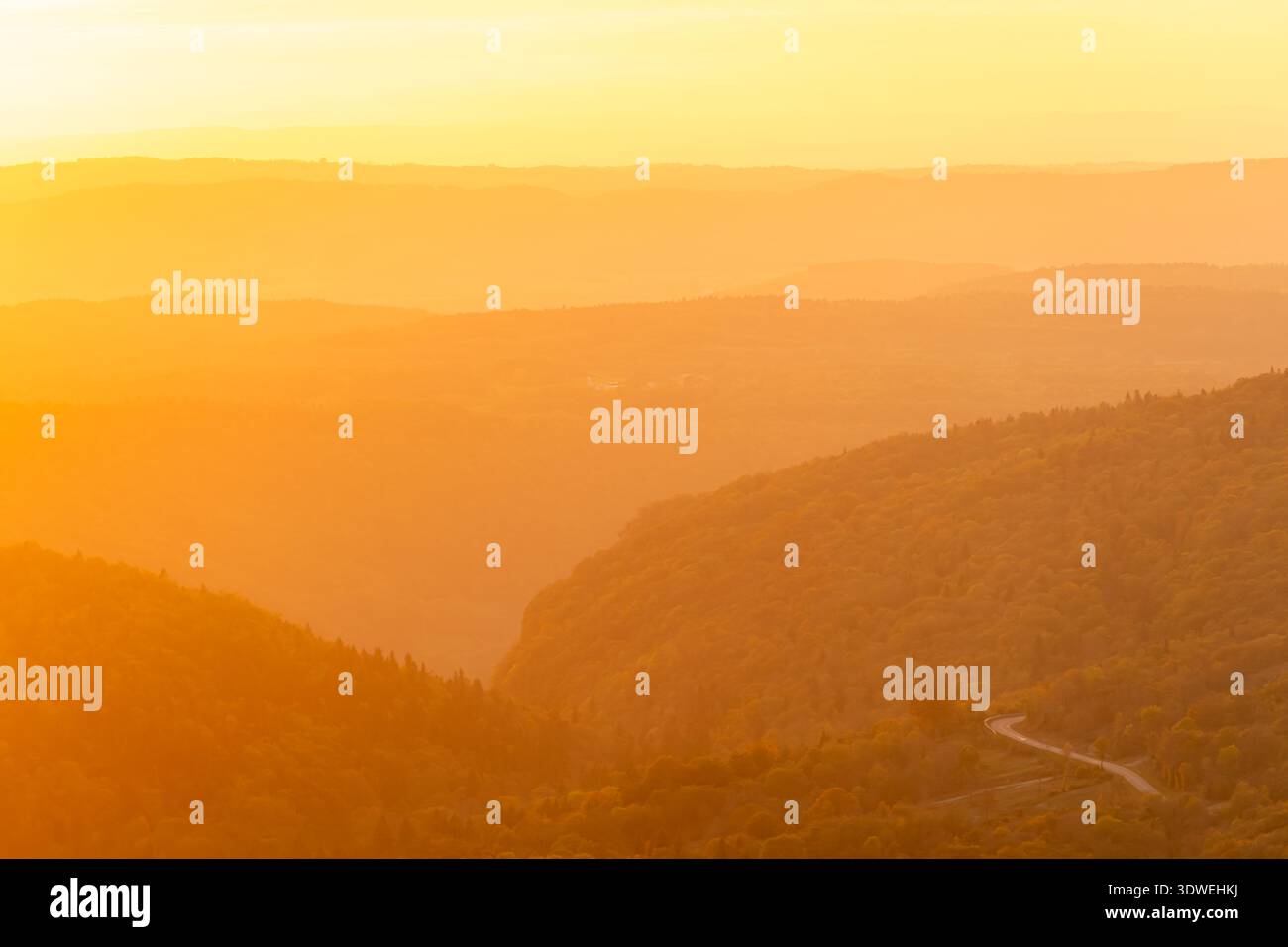 Vista mozzafiato delle colline ondulate bagnate dal caldo bagliore di un sole che tramonta, con vivaci tonalità arancio e oro in tutto il paesaggio. Un sereno e t Foto Stock