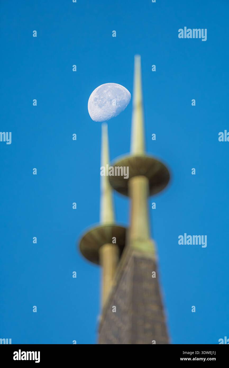 Una vista accattivante della luna posizionata sulle guglie di una cattedrale di Ginevra, adagiata su un cielo azzurro. Questa immagine unisce magnificamente celeste Foto Stock