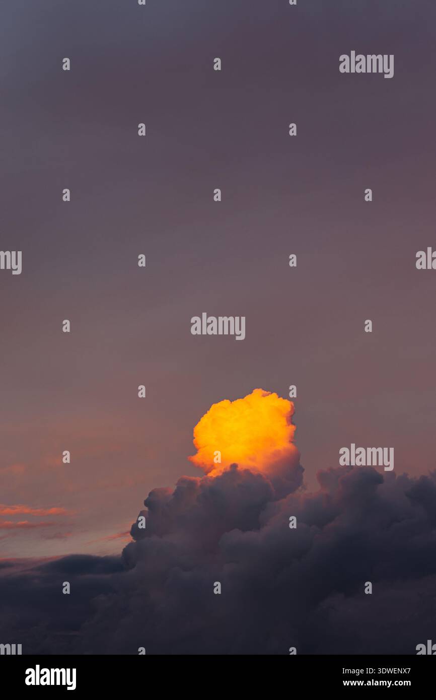 Una nuvola arancione illuminata dal sole che tramonta contro un tranquillo cielo serale viola, catturando la bellezza serena e il contrasto del colon della natura Foto Stock