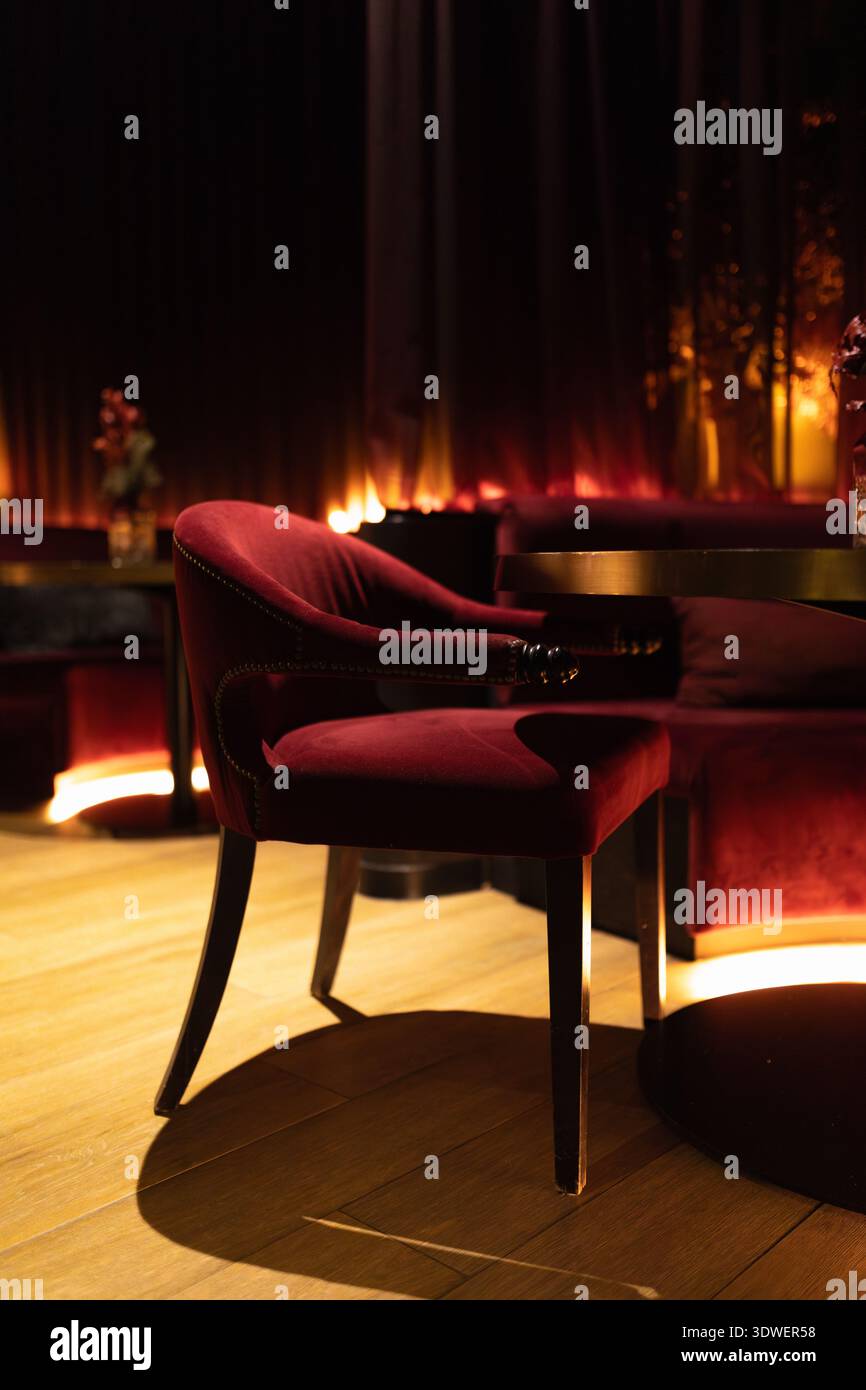 Sofisticata sala cocktail con poltrone in velluto sotto una luce calda e soffusa. I tavolini creano la scena per un'atmosfera intima ed elegante tipica Foto Stock