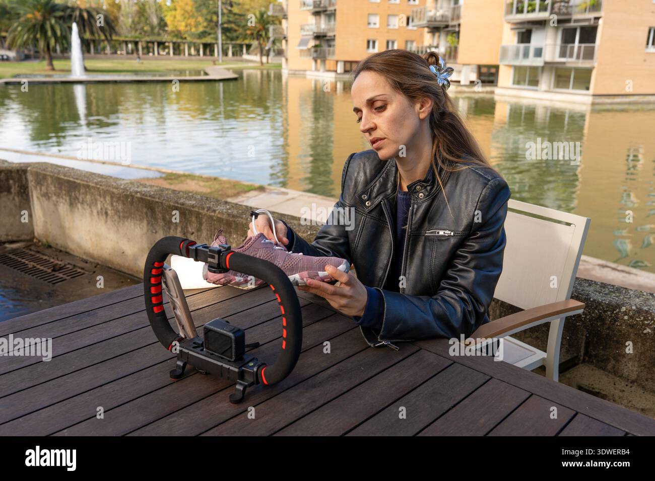 Un creatore di contenuti si concentra sulla presentazione di sneakers a piedi nudi durante le riprese in un pittoresco ambiente lacustre. Perfetto per nomadi digitali e influencer Foto Stock