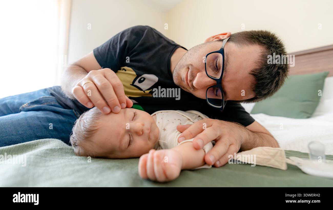 Un padre trascorre amorevolmente del tempo di qualità con il suo bambino, sdraiato insieme su un comodo letto. La scenografia cattura l'essenza dell'Unione padre-figlio in un Foto Stock