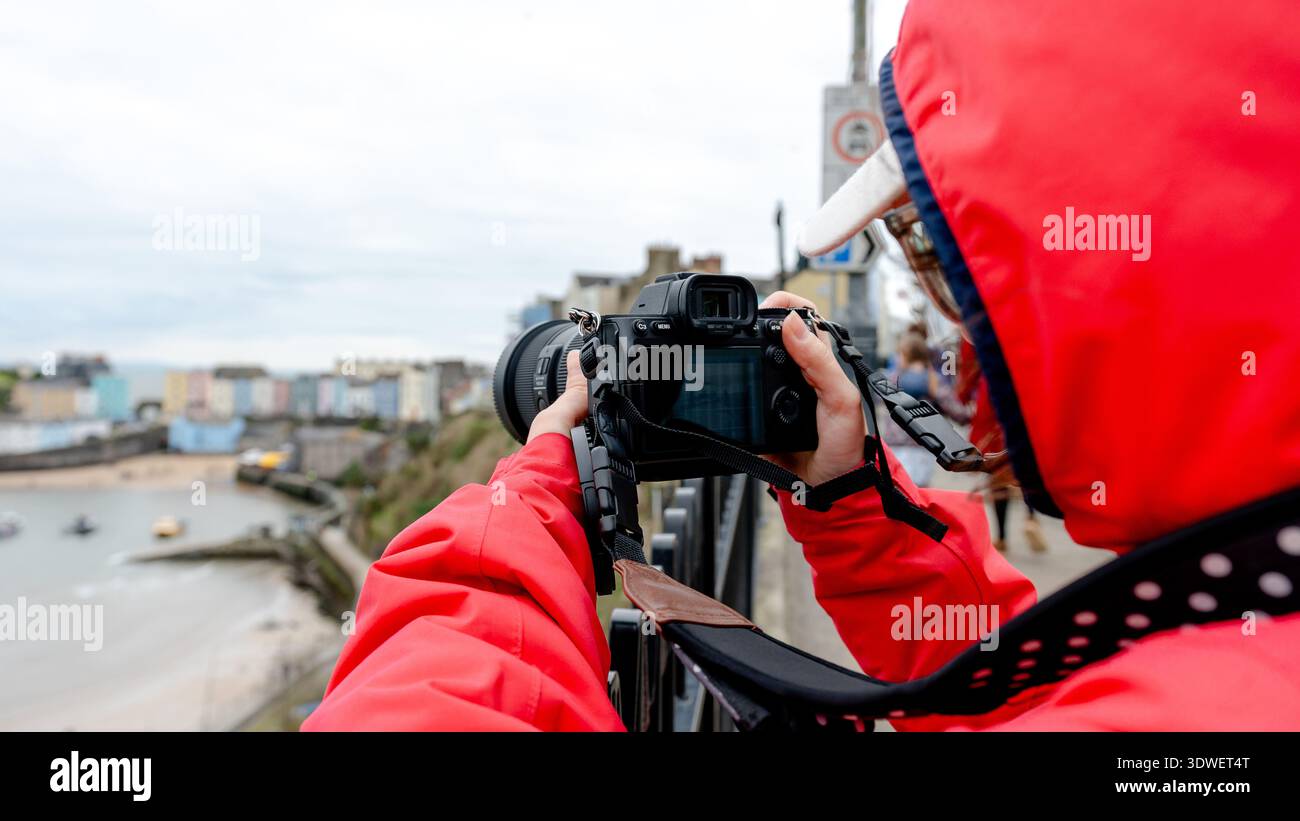 Un fotografo con una giacca rossa cattura la bellezza panoramica di Tenby, una città costiera nella baia di Carmarthen. Notevoli sono le sue mura del XIII secolo e colorate Foto Stock