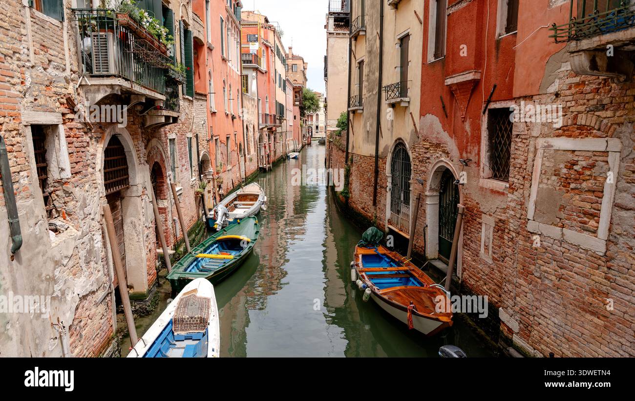 Un pittoresco canale veneziano nel quartiere di San Polo con colorati edifici storici e piccole barche dei proprietari locali lungo il corso d'acqua, riflessi Foto Stock