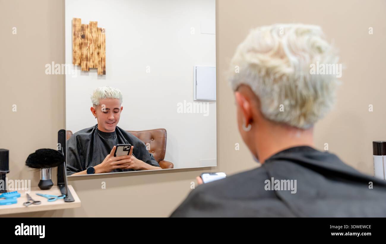 Una persona è al barbiere, seduta di fronte a uno specchio con i capelli appena sbiancati. Strumenti e prodotti sono visibili, creando un professionista e un mese Foto Stock