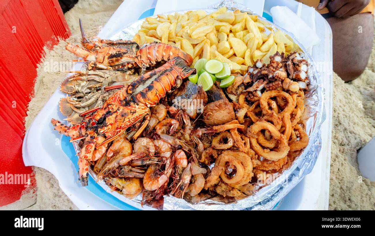 Un vivace piatto di pesce della Tanzania con aragosta alla griglia, gamberi, calamari e patatine fritte, servite con spicchi di lime, evoca il ricco sapore costiero Foto Stock