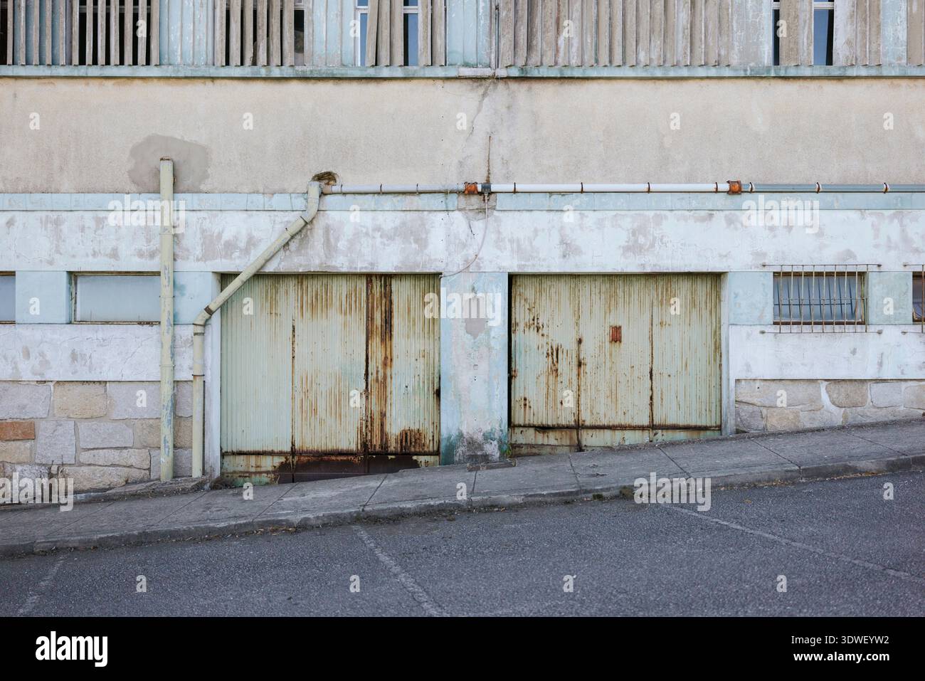 Due porte di garage arrugginite e intemperie in un vecchio edificio urbano. Le texture ruvide e i colori tenui trasmettono l'età e il carattere, aggiungendo un tocco rustico e di alta qualità Foto Stock