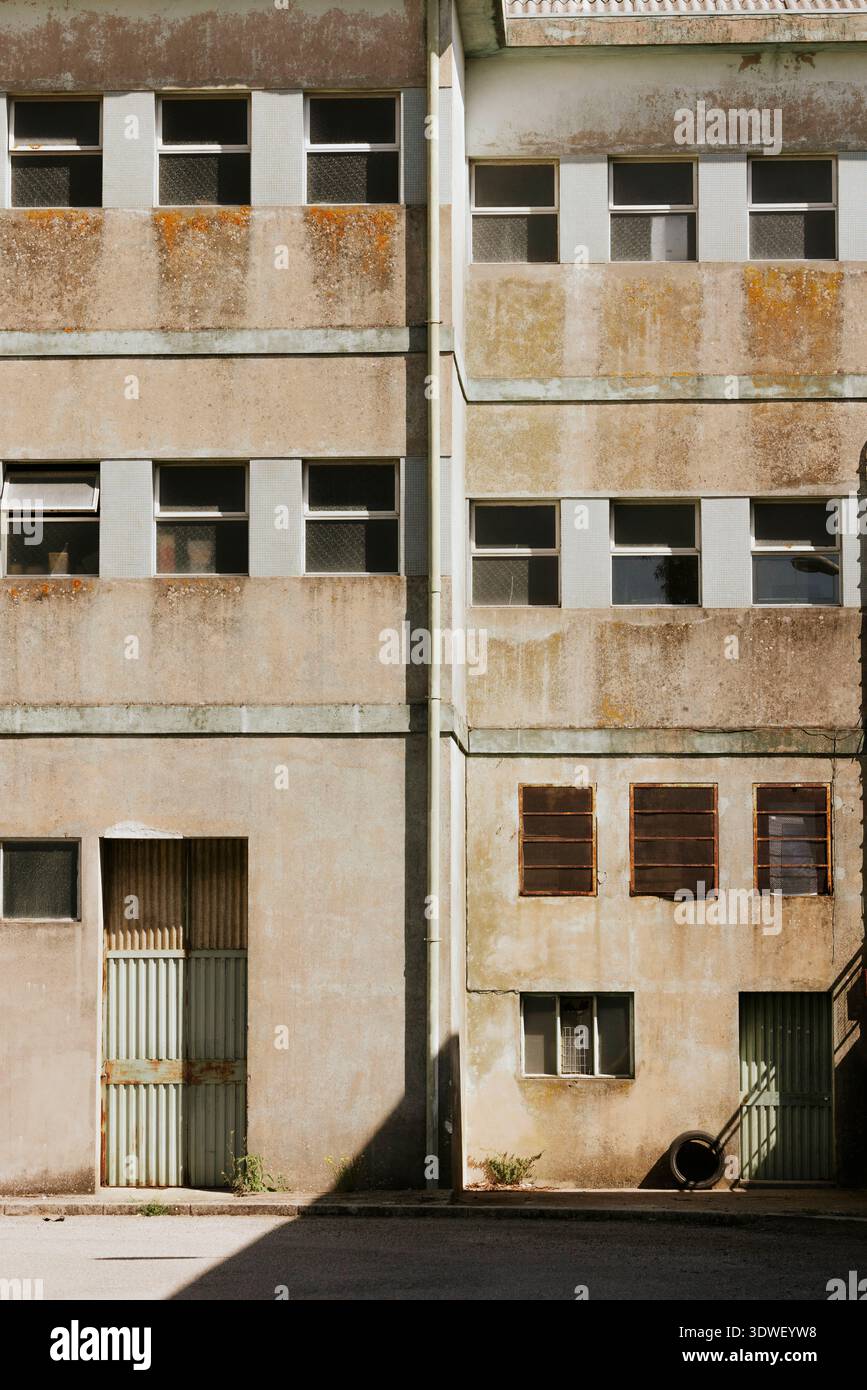 Un edificio industriale abbandonato con una facciata usurata e finestre multiple, che cattura un esterno duro e intempestivo. La struttura presenta ruggine e vi Foto Stock