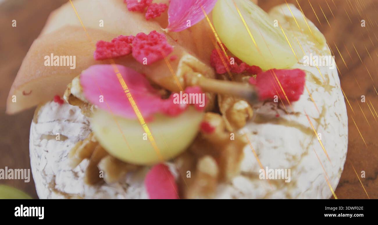 Mostra il brie sormontato da noci, metà uva verde, petali rosa su tavola di legno con luce dorata Foto Stock