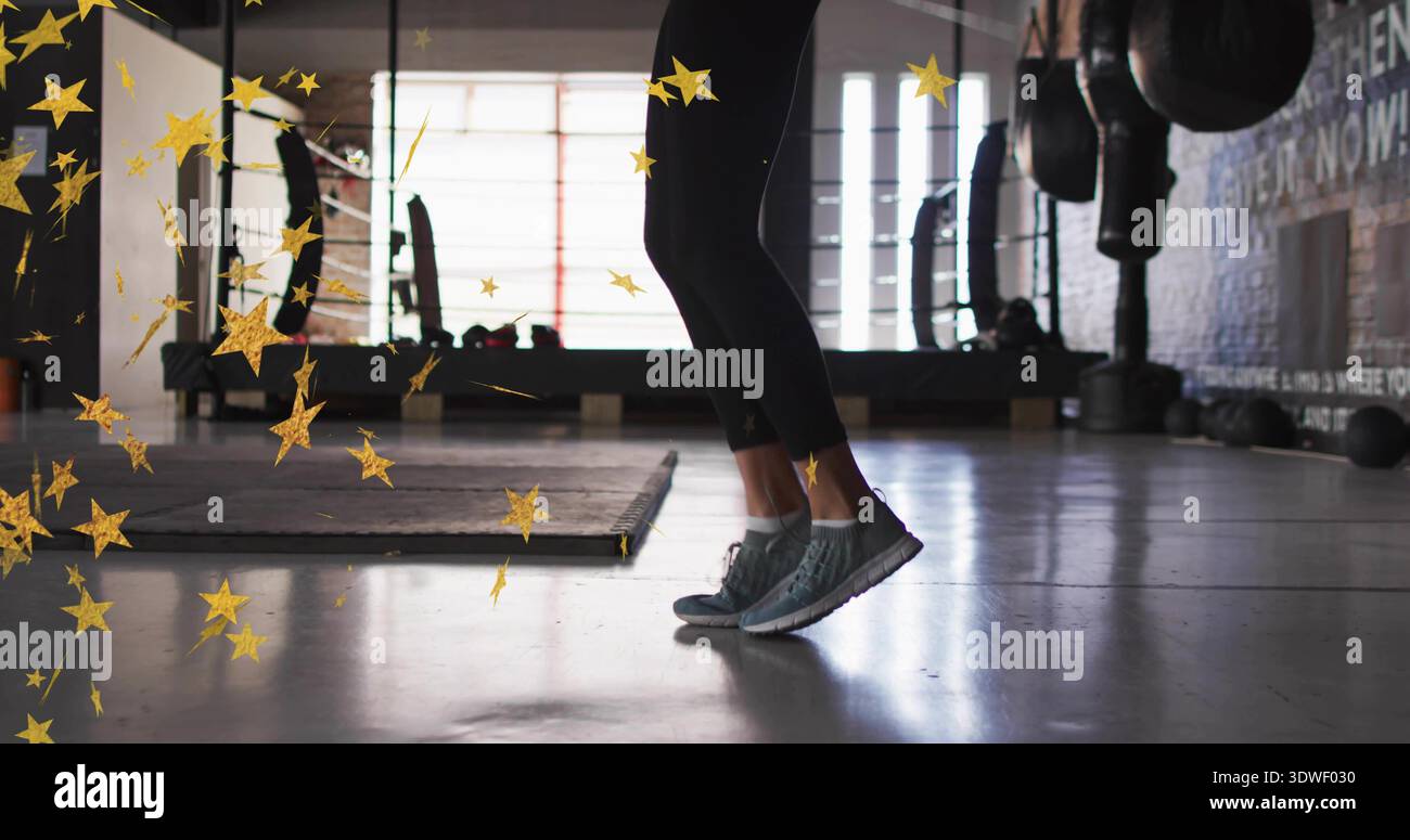 Saltando le gambe e i piedi della donna che si alzano sopra il pavimento della palestra, indossando leggings neri e scarpe grigie Foto Stock