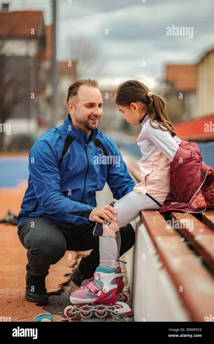 Padre che insegna alla figlia come legare le pale a rotelle all'aperto Foto Stock