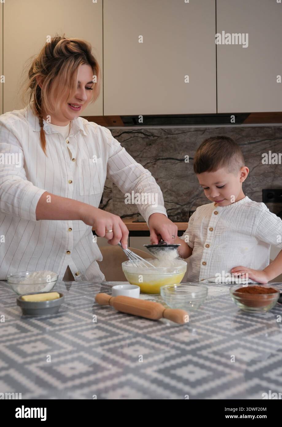Una madre e un bambino adorano il tempo di cottura in cucina. La scena cattura la gioia e il calore della genitorialità, enfatizzando l'amore, il sostegno e fami Foto Stock