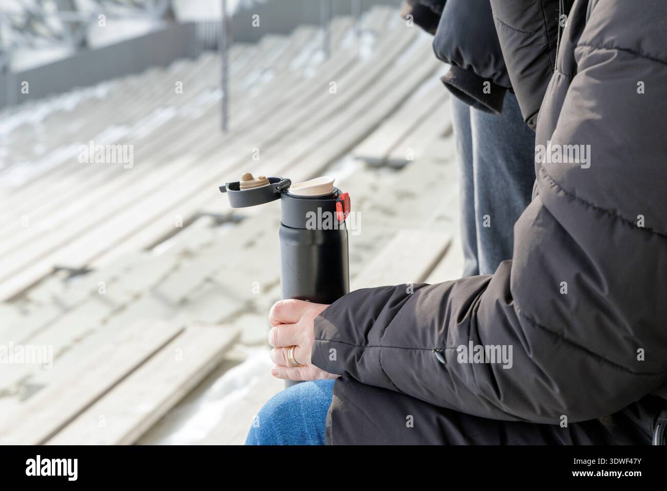Primo piano di mani che tengono in mano una tazza termica nera durante un evento invernale all'aperto. Un intimo momento di idratazione e calore durante le fredde attività stagionali. Foto Stock