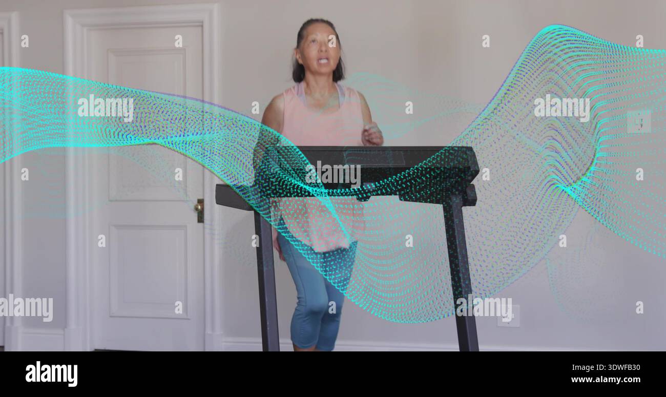 Donna anziana che cammina in rosa, leggings blu con tapis roulant a casa con copertura a onde turchesi Foto Stock