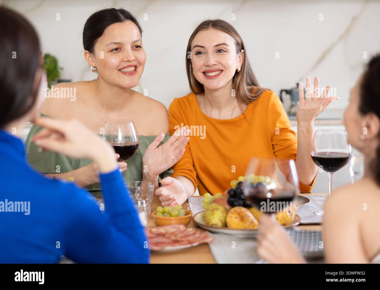 Quattro donne sono sedute a tavola, si godono cibo e vino, chiacchierano, parlano, ridono. Foto Stock