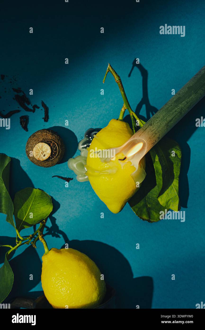 Un limone vibrante si trova su un impressionante sfondo blu, accompagnato da una candela ardente e da un oggetto scuro. Questa moderna composizione di natura morta crea un Foto Stock