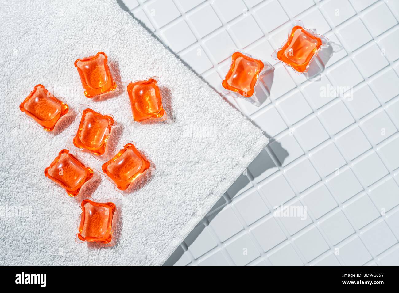 Le capsule per bucato di colore arancione luminoso sono esposte su un asciugamano bianco e una superficie piastrellata, evidenziando la loro praticità e il design moderno per un'efficienza maggiore Foto Stock