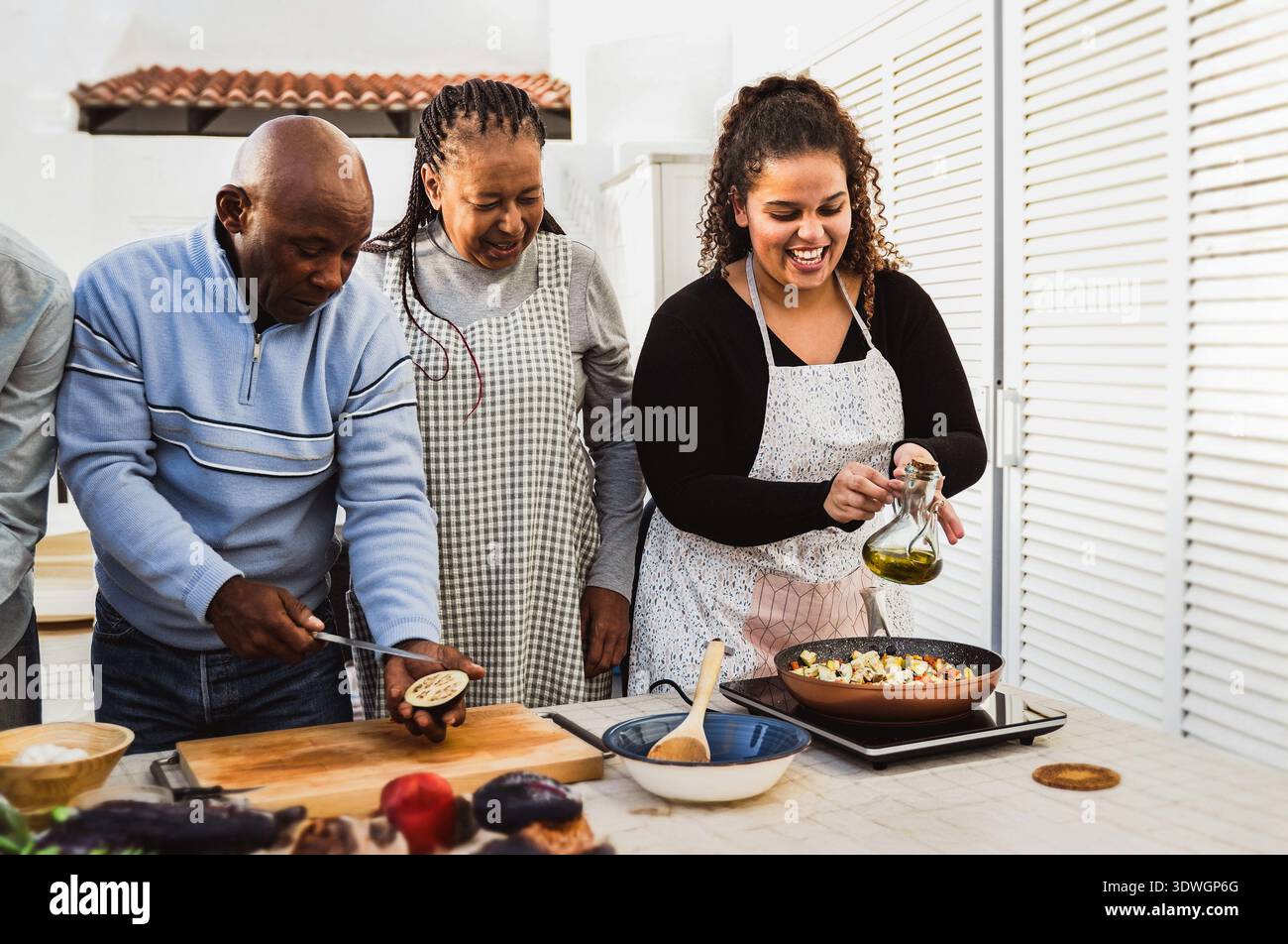 Famiglia africana felice che prepara insieme pasti vegetariani nel patio di casa - cucina all'aperto e concetto di legame familiare Foto Stock