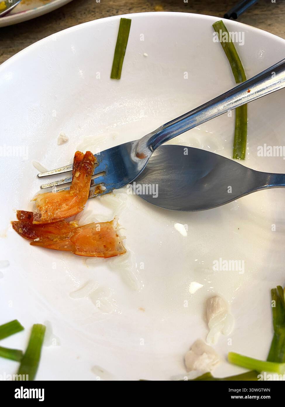 Piatto bianco con gamberi e cipolla verde rimasti, con forchetta e cucchiaio posizionati lateralmente, a indicare un pasto finito di recente Foto Stock
