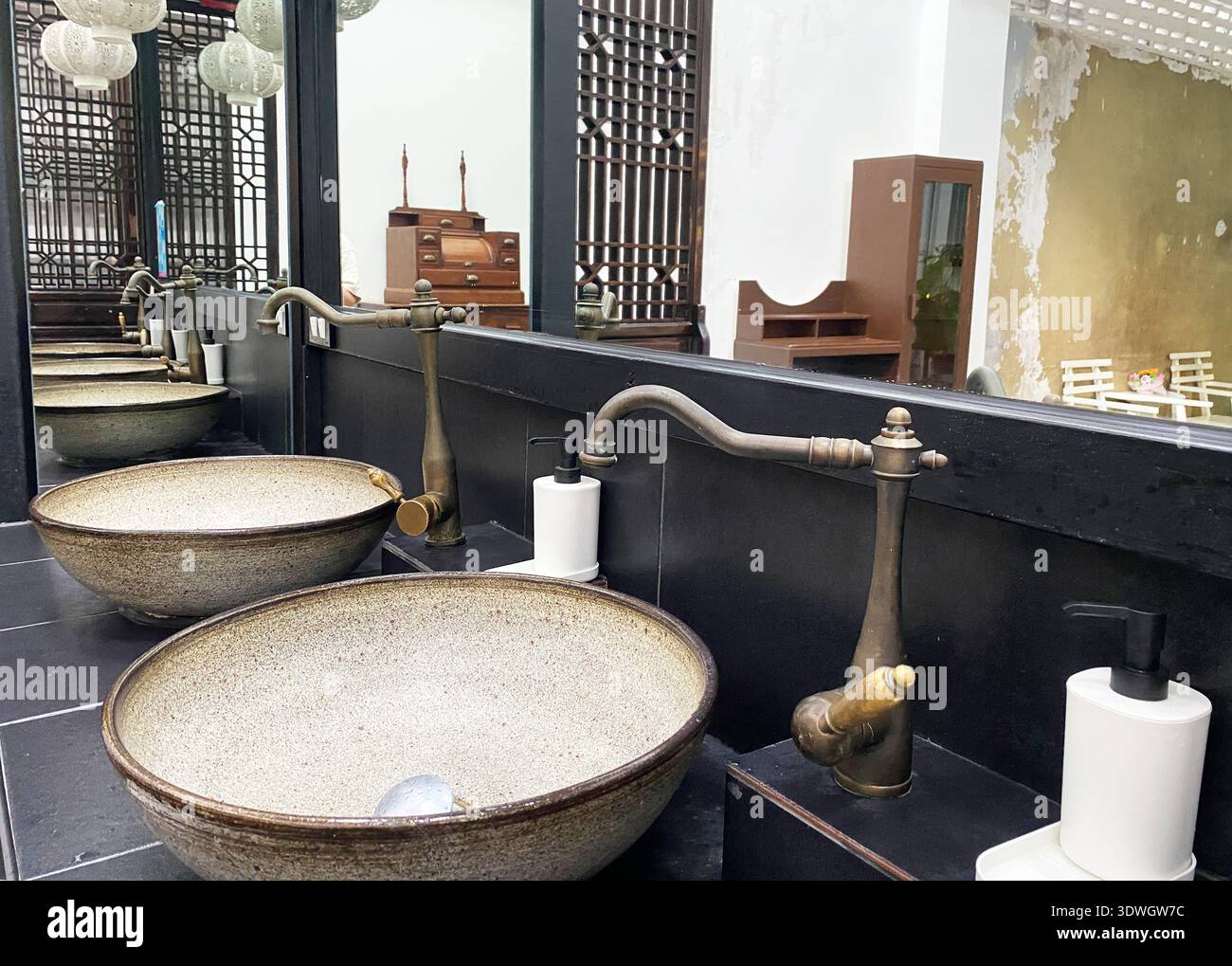L'interno del WC in stile asiatico presenta lavandini rotondi in pietra con rubinetti vintage, accenti in legno e una disposizione spaziosa, illuminati da luce naturale Foto Stock
