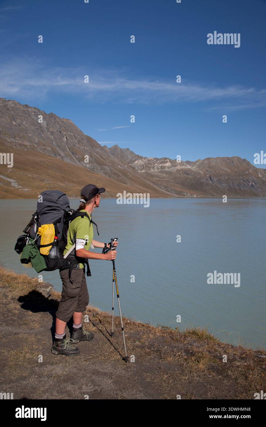 Un escursionista si erge con un grande zaino su un sentiero di montagna che si affaccia sulle acque glaciali del Lac des Dix, Vallese, Svizzera. Foto Stock