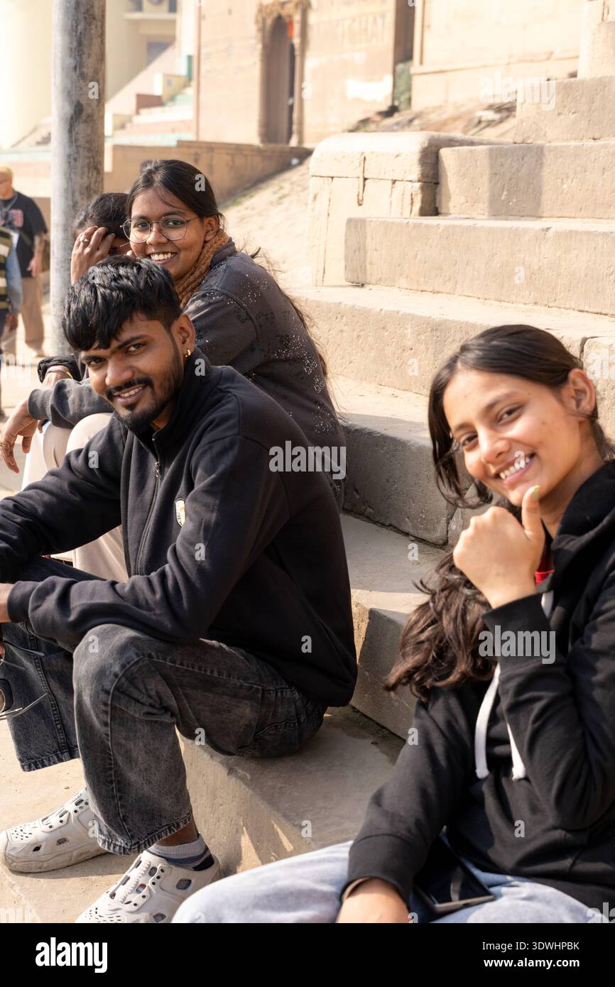 Giovani sorridenti seduti su gradini di pietra che si godono una giornata di sole a Varanasi, India. Foto Stock