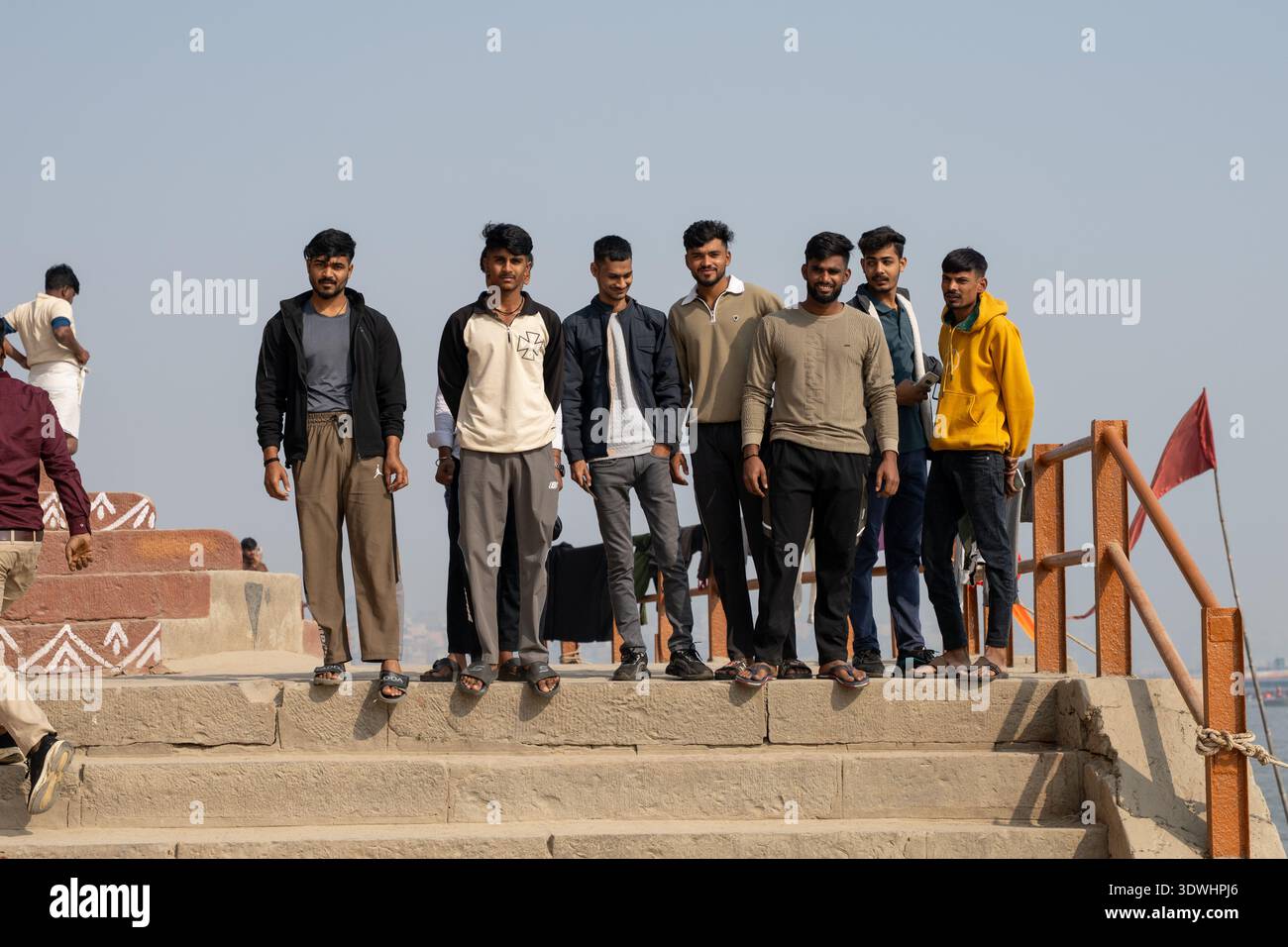Un gruppo di giovani uomini sta su gradini di pietra a Varanasi, in India, sotto un cielo limpido durante il giorno. Foto Stock