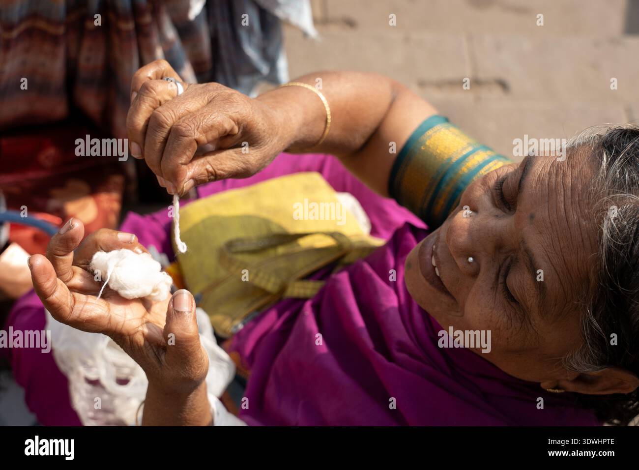 Una donna anziana di Varanasi, India, gira sapientemente il filo di cotone a mano in un abbigliamento tradizionale. Foto Stock
