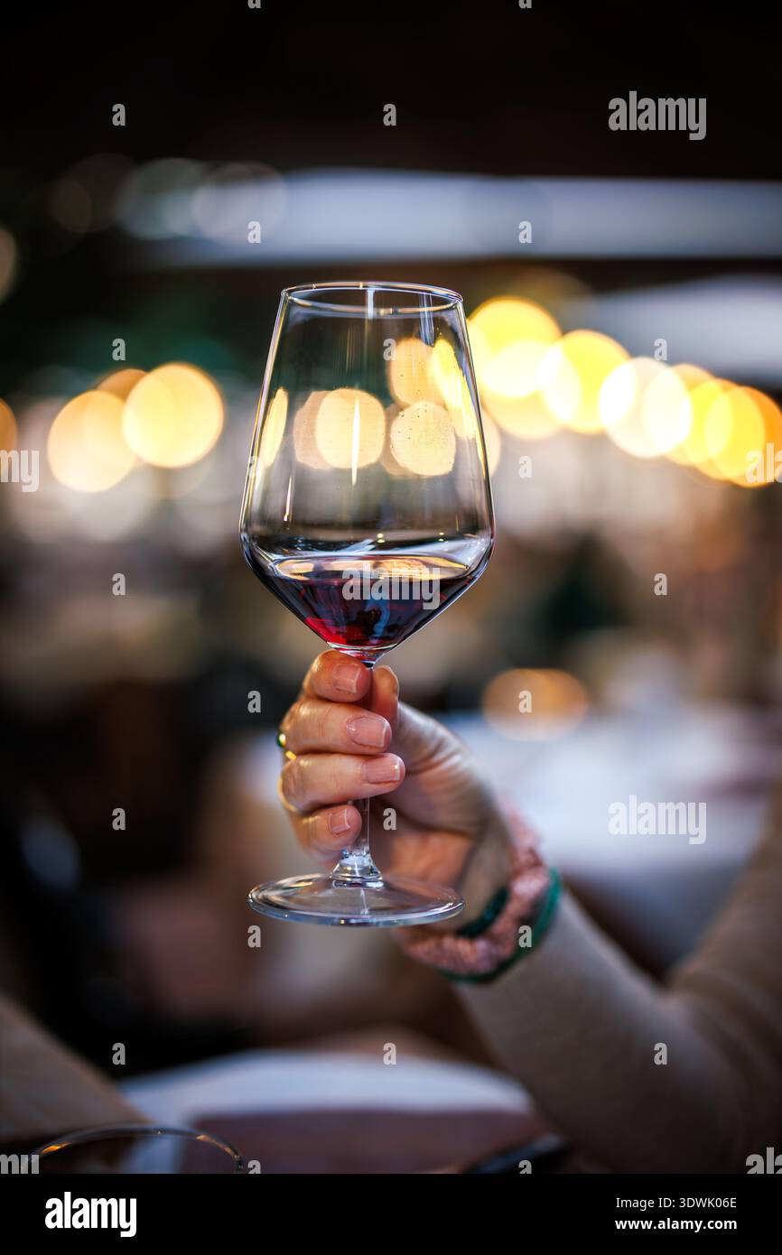 Brindisi celebrativo con vino rosso. Donna che tiene in mano la wineglass al ristorante durante la cena. Bere alcolici al bar Foto Stock