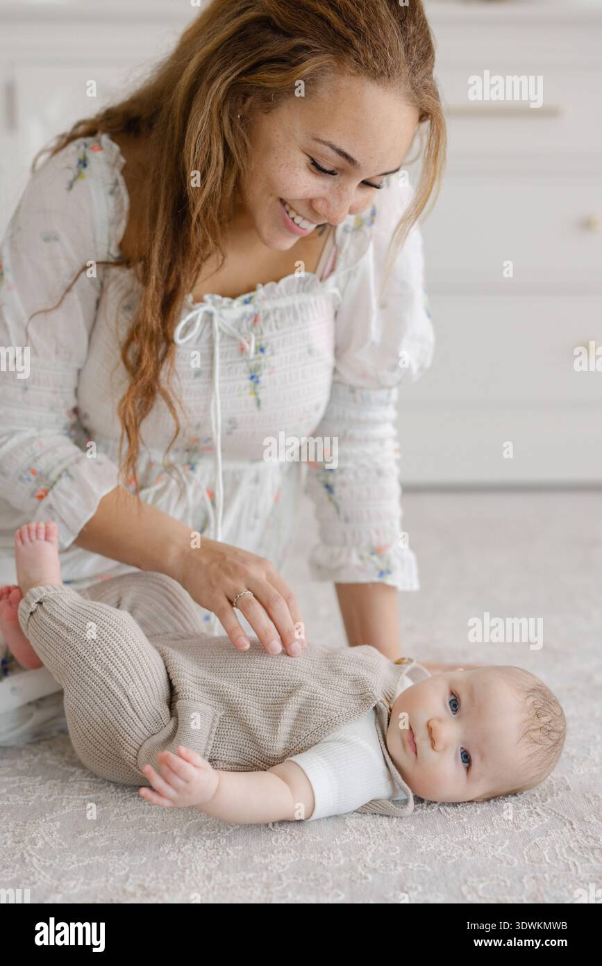 Sorridente madre di razza mista che gioca con il bambino sul pavimento della nursery Foto Stock