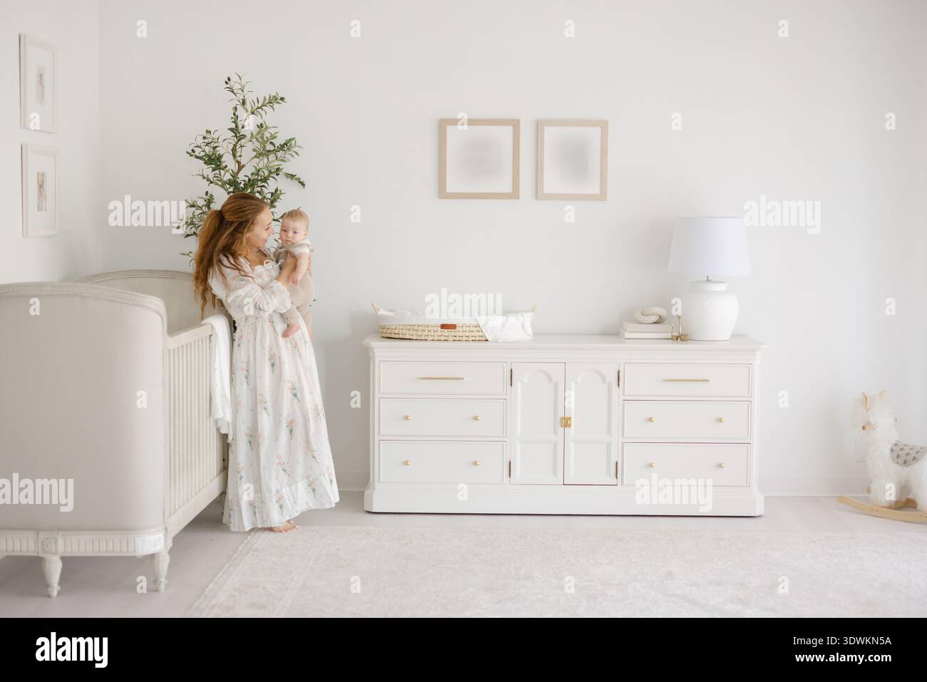 Mamma e bambino in un vivaio luminoso con olivo e culla Foto Stock