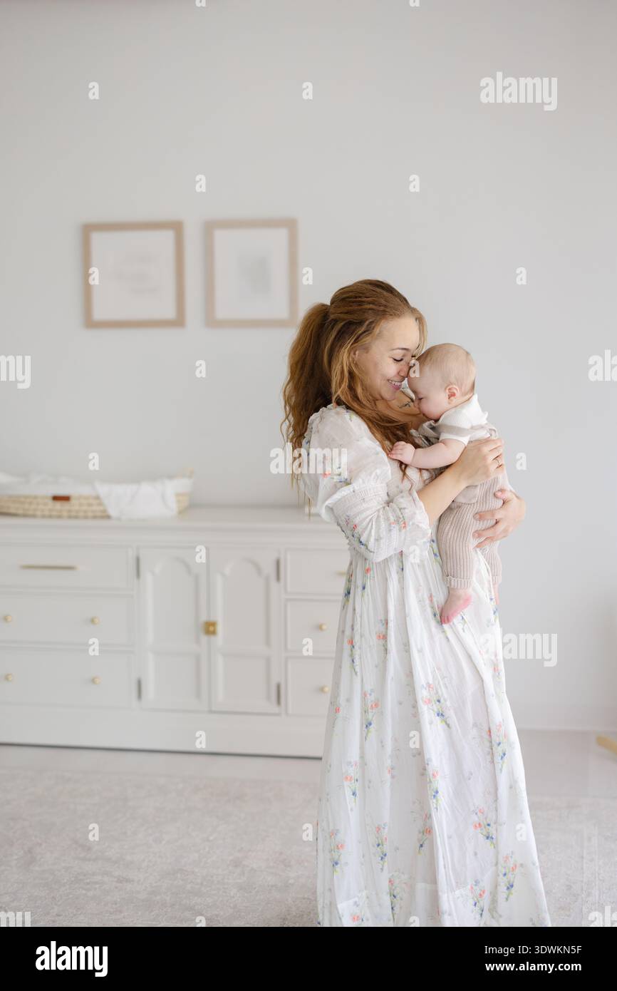 Mamma nuzzling e bacia il bambino nella nursery bianca Foto Stock