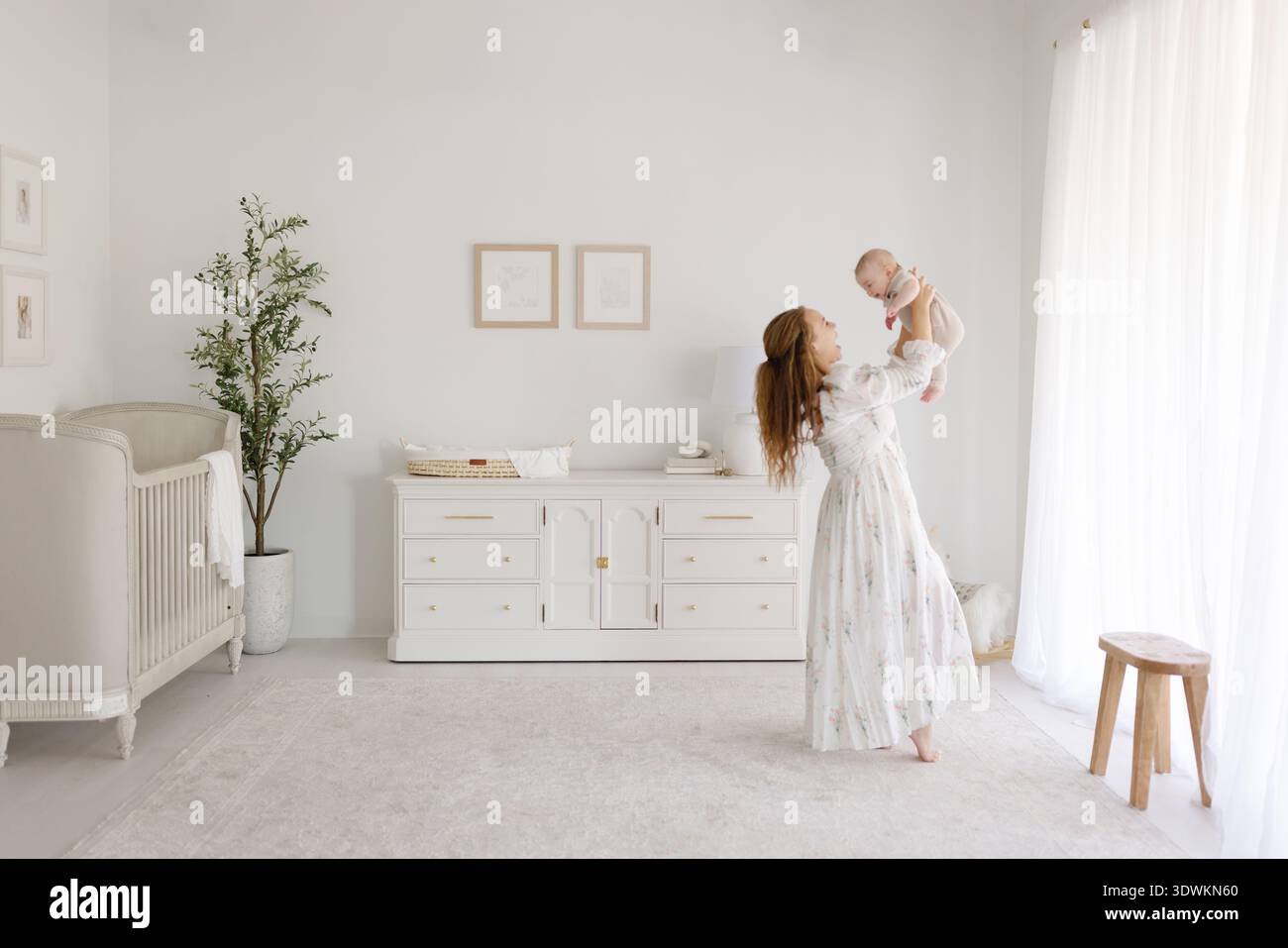 Allegra madre che solleva il bambino nell'aria in un vivaio bianco brillante Foto Stock