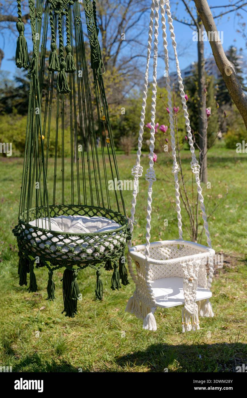 Sedie a culla in macrame intrecciato in colori bianco e nero su sfondo verde. Concetto di home design bohémien, arte tessile artigianale e co Foto Stock