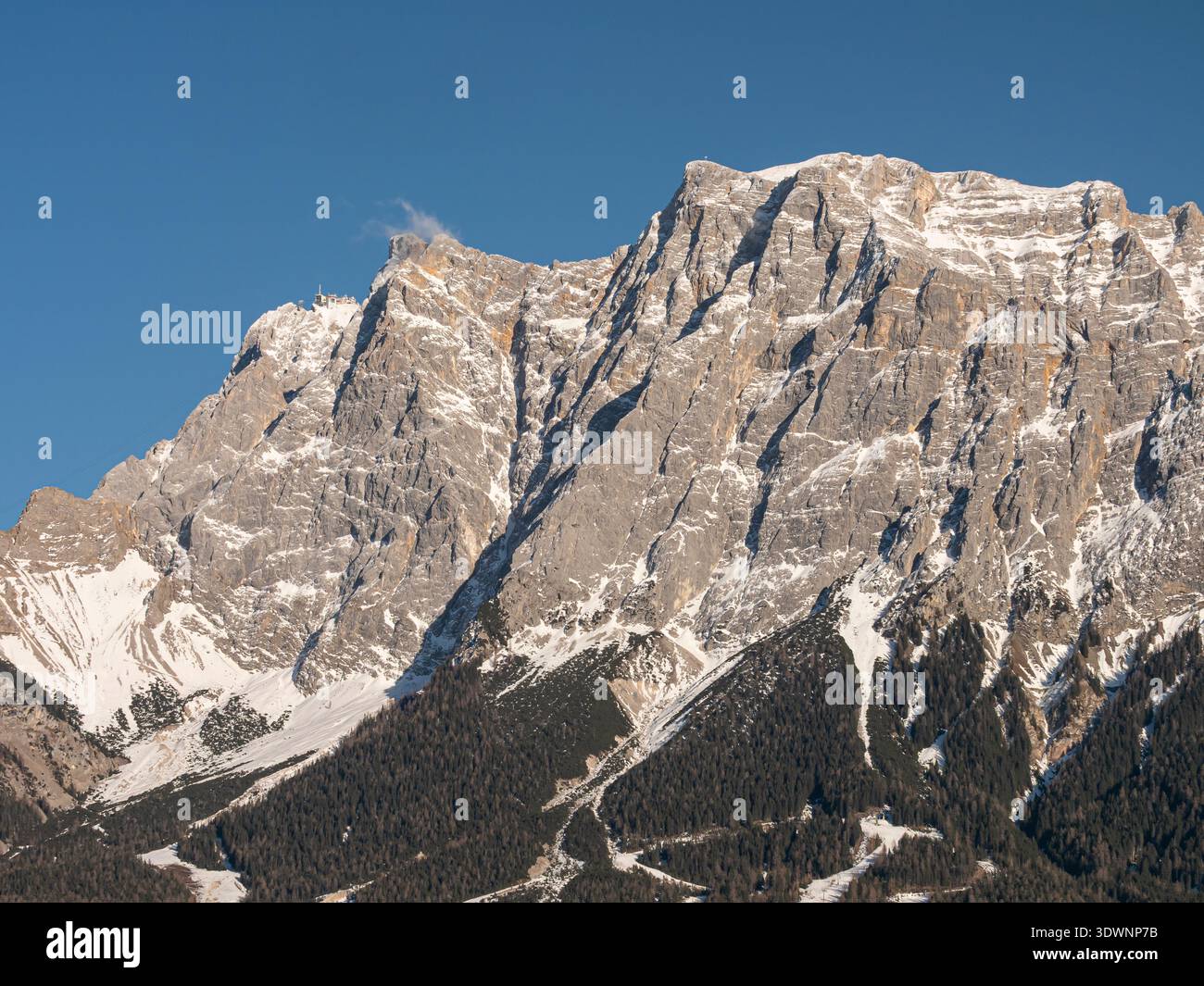 Aspre scogliere alpine con cima innevata e pendii boscosi in piena luce del giorno Foto Stock