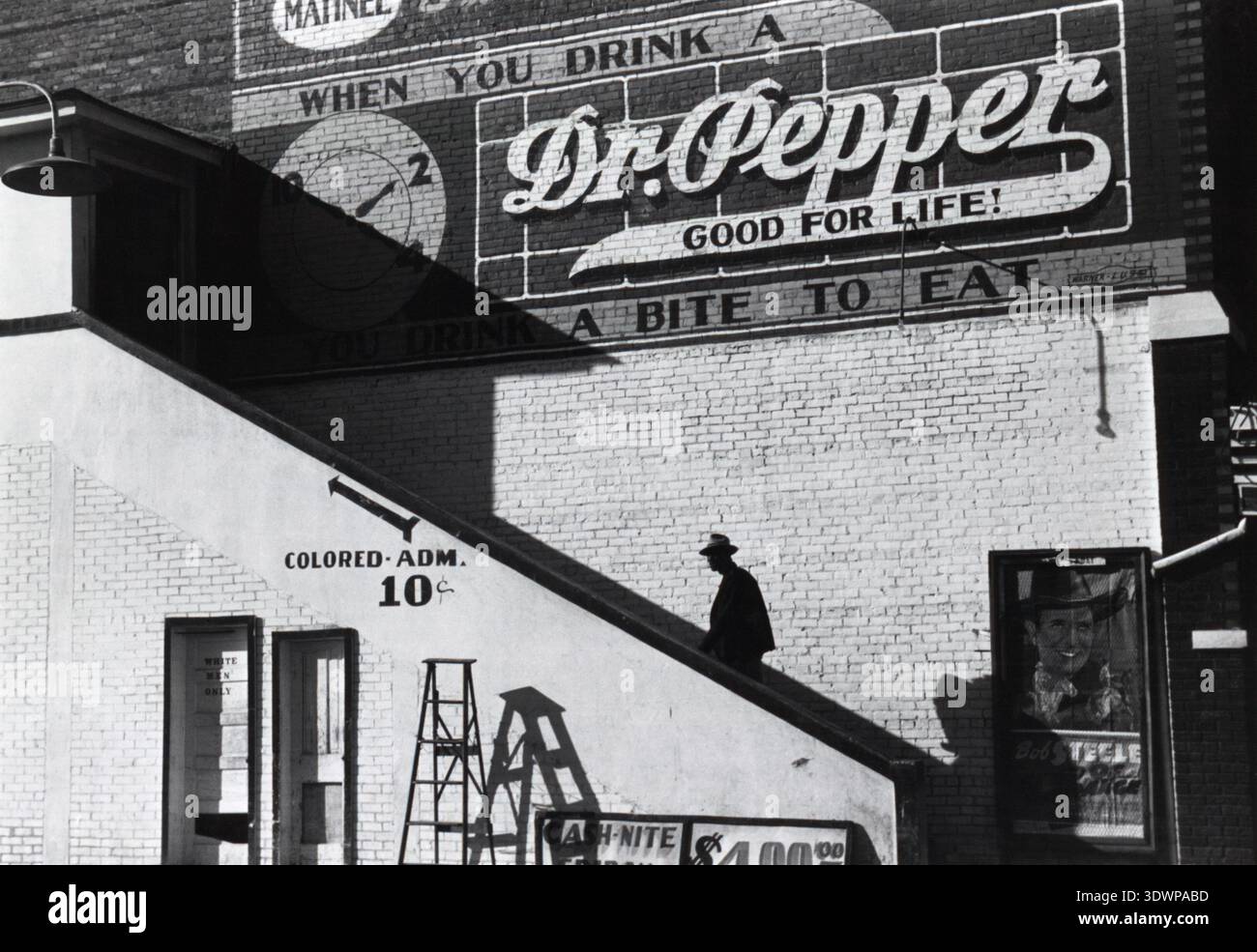 Questa potente fotografia del 1939 di Marion Post Wolcott cattura un afroamericano che sale al "ADM COLORATO". Ingresso al Crescent Theatre di Belzoni, Mississippi. L'immagine illustra in modo inequivocabile le realtà della segregazione razziale durante l'era Jim Crow, con un cartello "SOLO UOMINI BIANCHI" visibile anche vicino a un ingresso inferiore, giustapposto a una pubblicità del Dr. Pepper sul muro di mattoni. Foto Stock