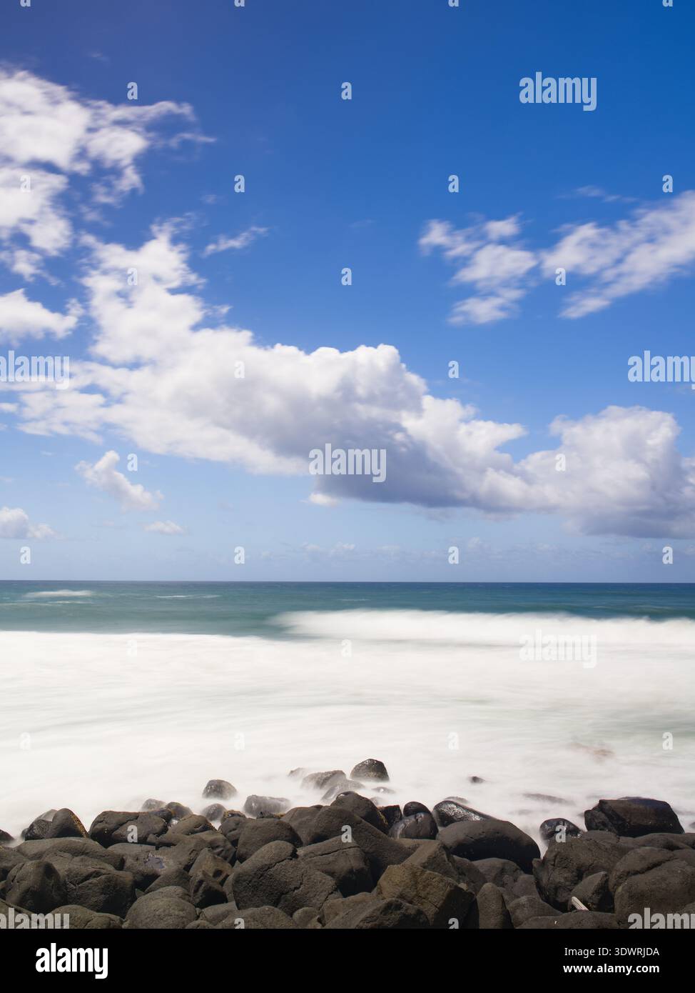 Lunga esposizione su spiaggia rocciosa con cielo blu e parzialmente nuvoloso Foto Stock
