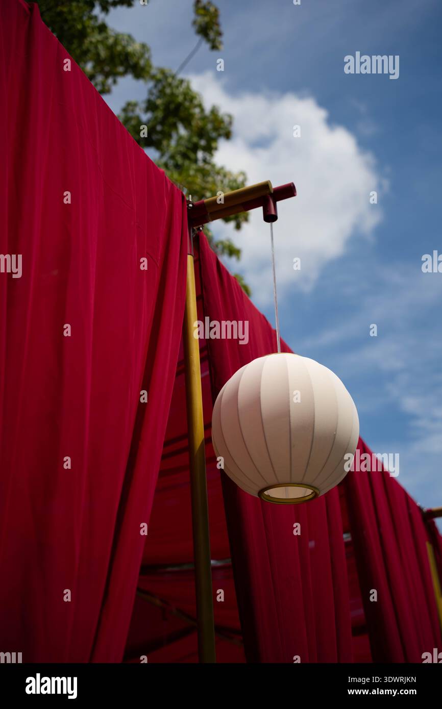 Colorate installazioni decorative di lanterne appese sopra una strada di un'antica città fotografate da un'angolazione bassa contro il cielo blu e le nuvole. Foto Stock