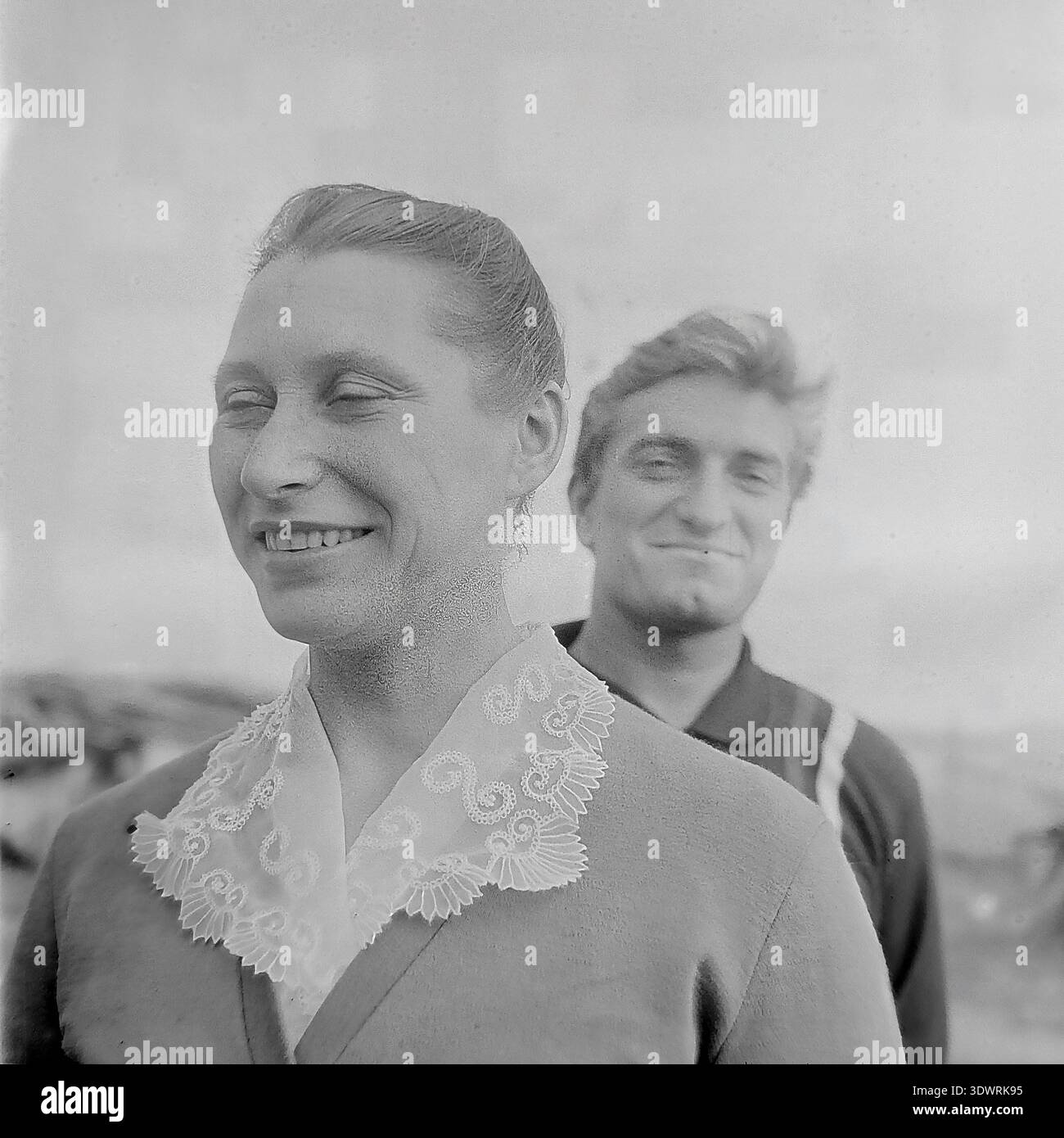 Storico ritratto in bianco e nero degli anni '1970 cattura due giovani lavoratori agricoli sorridenti presso l'impresa statale Donrybkombinat nel distretto di Slavyansk, RSS Ucraina, URSS. La donna in primo piano, che indossa una camicetta leggera con un elegante colletto in pizzo, guarda lontano con un'espressione gioiosa, mentre un giovane sta dietro di lei sorridendo dolcemente alla fotocamera. Questa autentica fotografia d'archivio mette in evidenza le connessioni umane, il cameratismo e l'atmosfera ottimistica e tranquilla della vita quotidiana nel tranquillo Donbass prima della guerra. Foto Stock