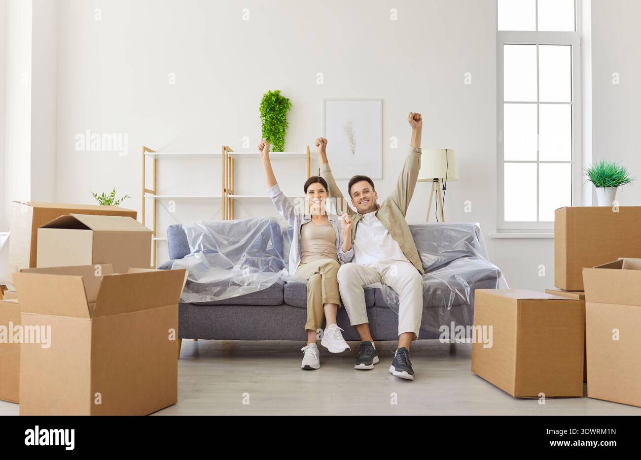 Felice giovane coppia che celebra l'acquisto di una nuova casa e si muove con le mani in alto Foto Stock