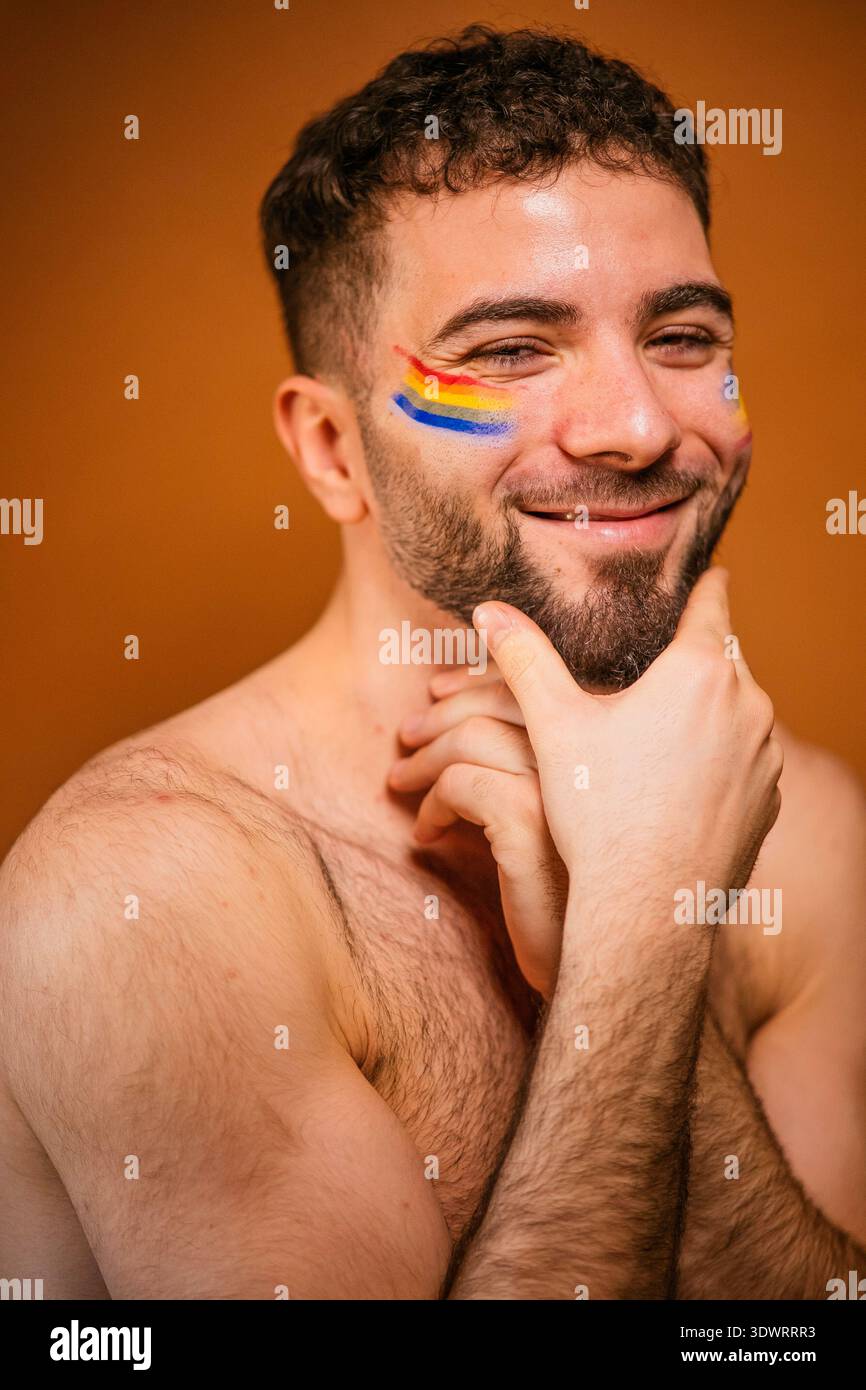 Uomo che sorride, mostra i colori della bandiera arcobaleno dipinti sulla guancia Foto Stock