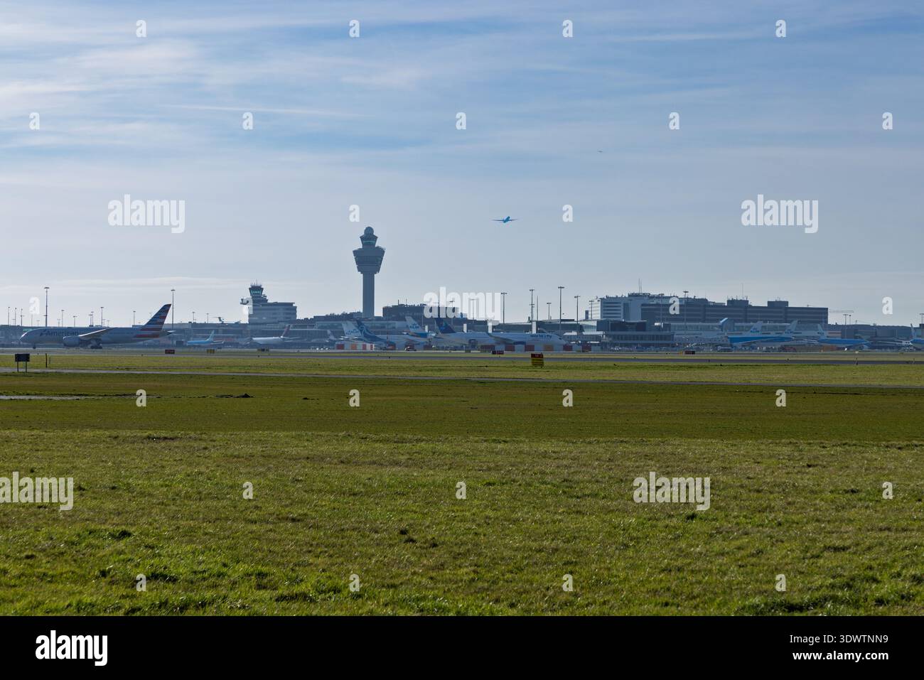Vista panoramica dell'aeroporto Schiphol di Amsterdam con torri di controllo, vari aerei parcheggiati sull'asfalto e un campo verde in primo piano. Schiphol Foto Stock