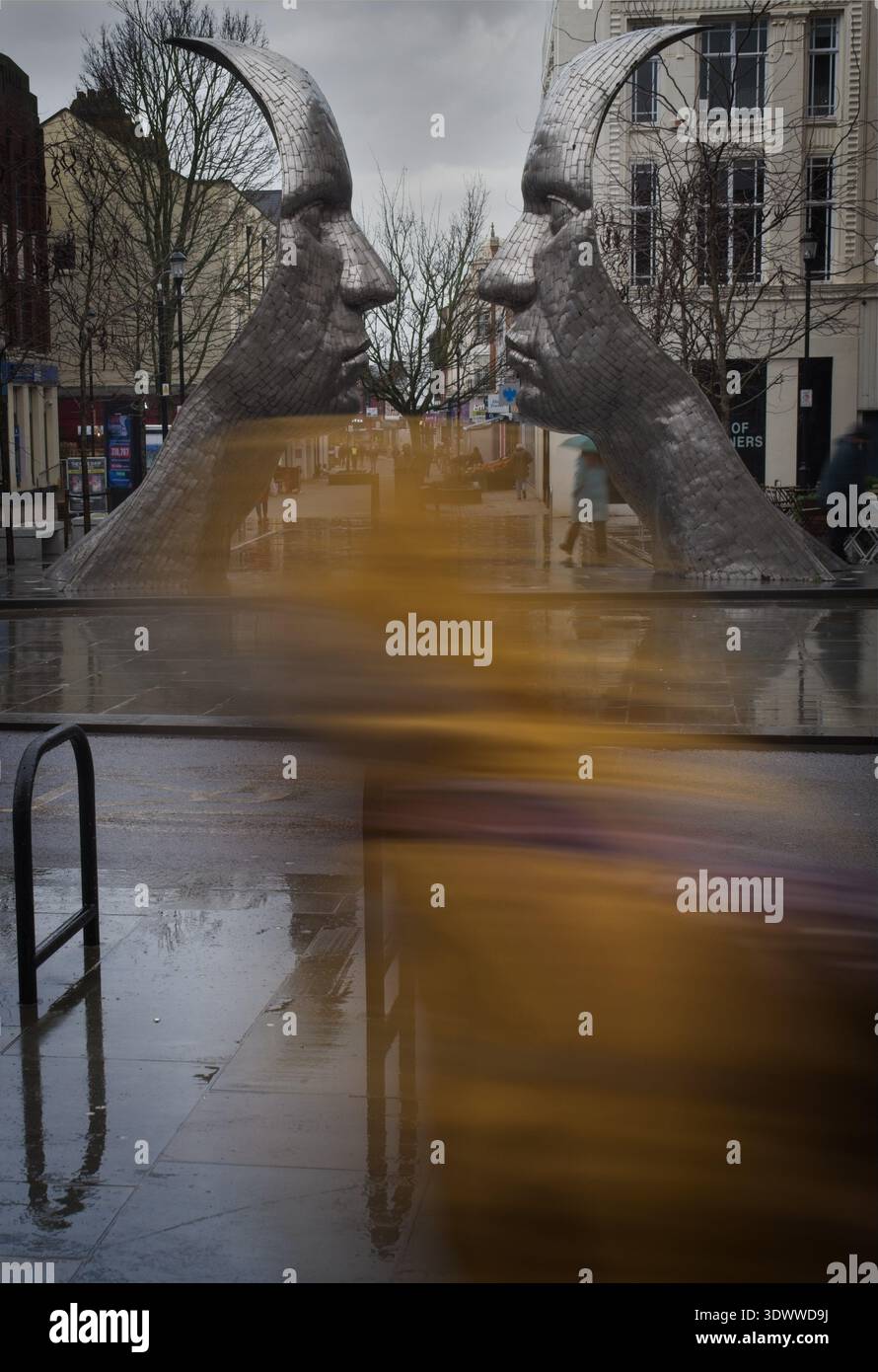 Affronta una scultura con una persona sfocata che passa accanto Foto Stock