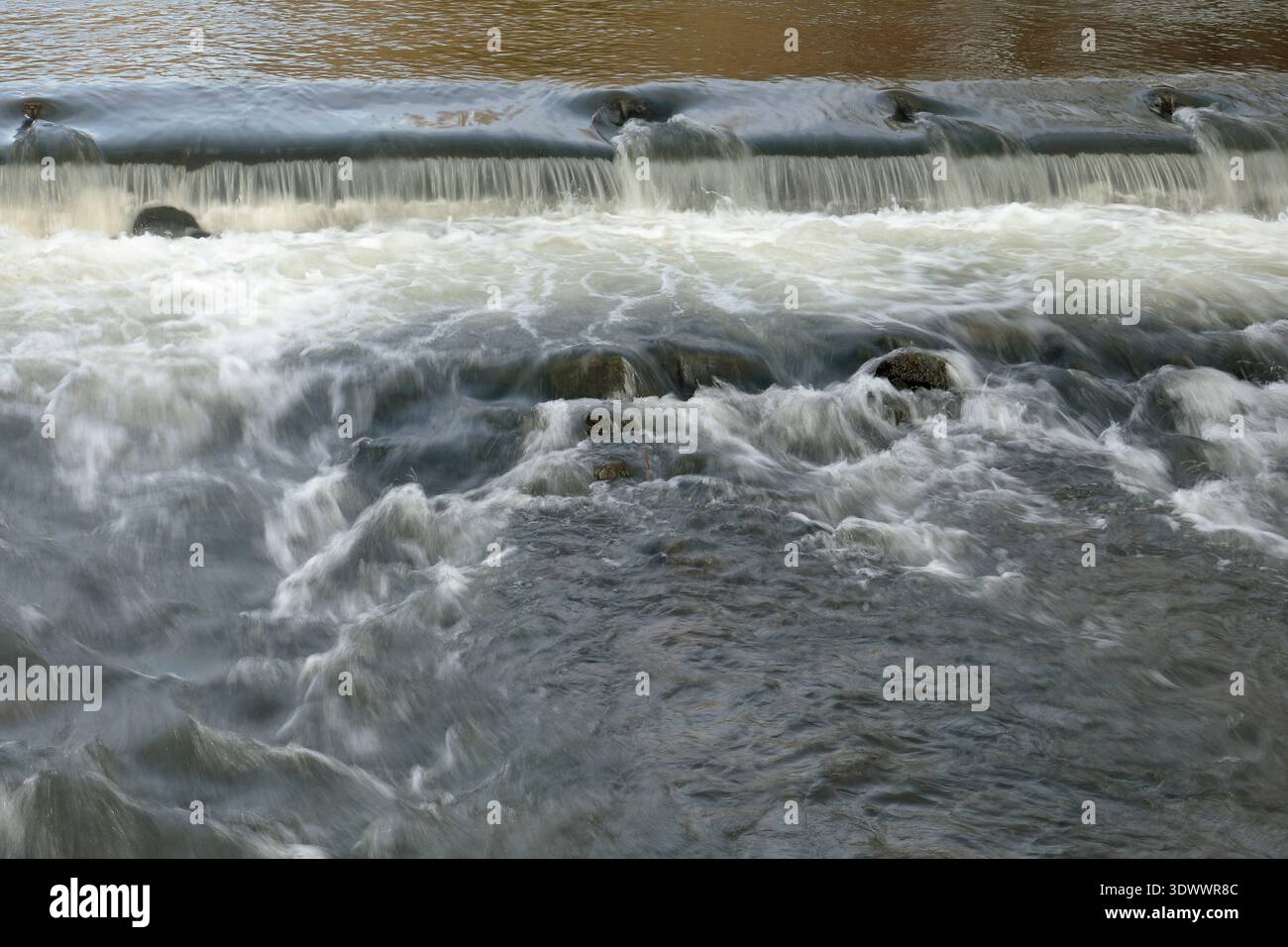 L'acqua scorre su una diga nel fiume Wye a Bakewell, utilizzando una velocità dell'otturatore lenta per mostrare i modelli nel flusso. Foto Stock