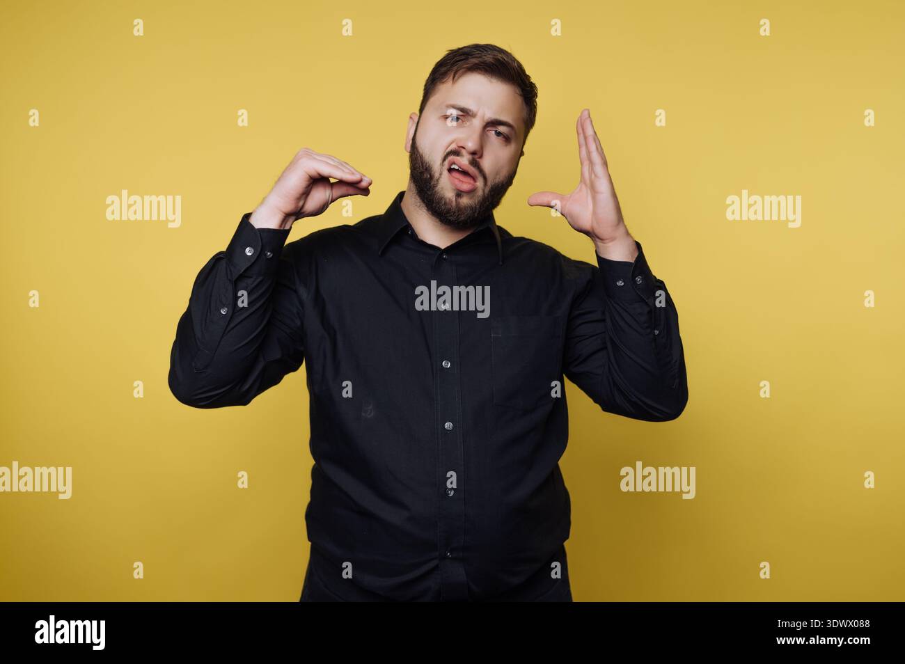 Un uomo con una camicia nera gesticola con passione, mostrando una serie di emozioni davanti a un vivace sfondo giallo. Le sue espressioni e il suo movimento Foto Stock
