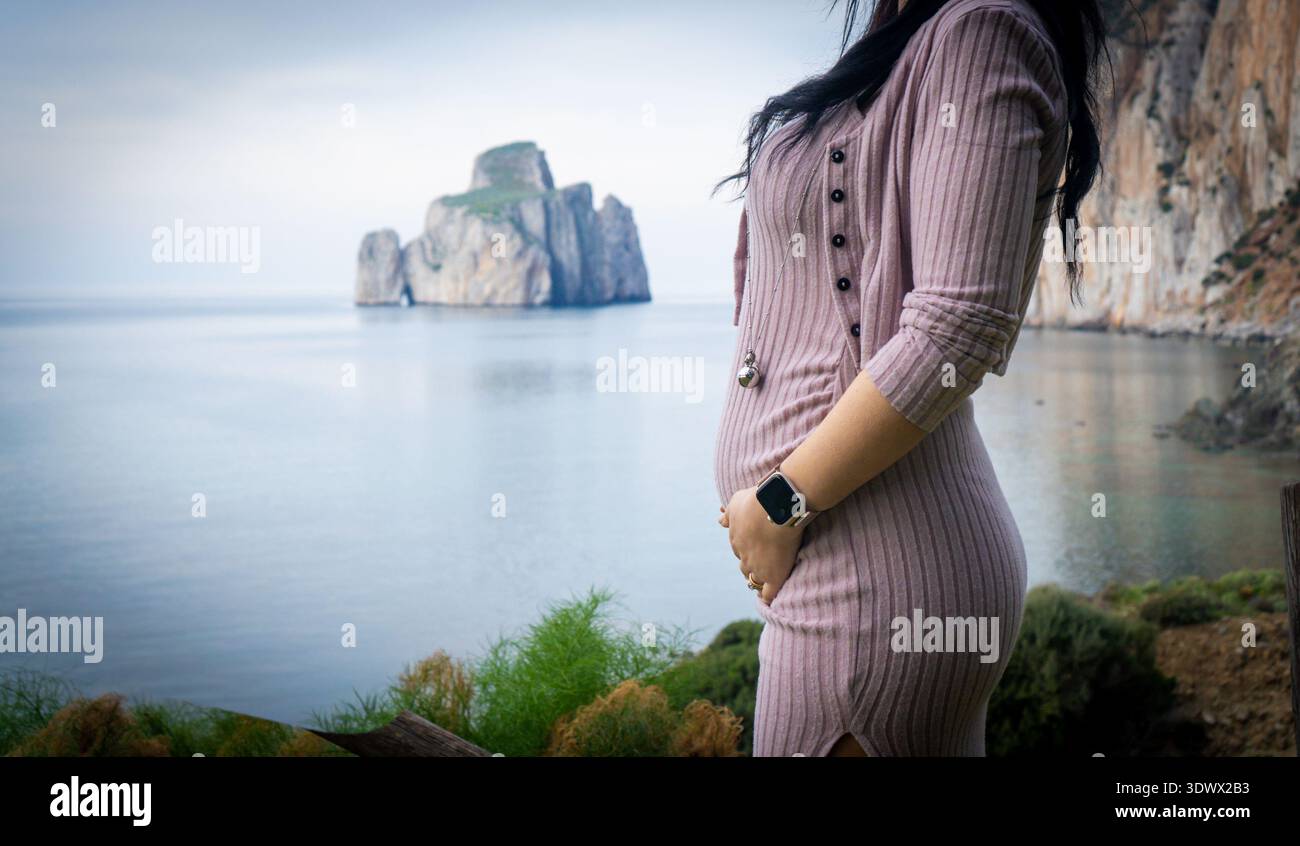 Donna incinta che tocca la pancia in riva al mare in Sardegna Foto Stock